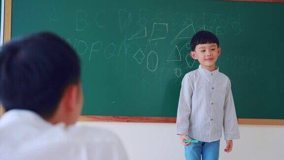 亚洲可爱的儿子在教室里和家长一起在黑板上画画小男孩在幼儿园做有趣的教育活动在黑板上写字母和数字和爸爸一起玩