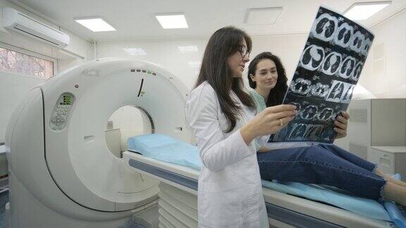 女医生放射科医生为年轻女性患者讲解CT扫描的良好效果用图像显示快照在现代临床CT扫描仪旁观察和分析CT扫描