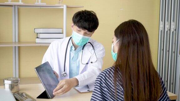 专业医生戴上外科口罩为病人讲解并展示带有肺部x光图像的屏幕笔记本电脑身穿大褂的医生在门诊病房与疑似感染冠状病毒(Covid-19)的患者交谈