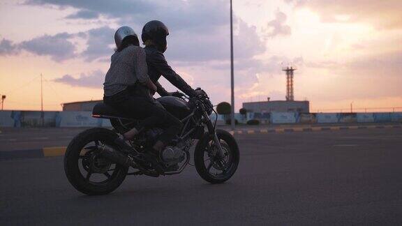 日落时分一对戴着头盔的年轻夫妇在城市里骑摩托车慢镜头