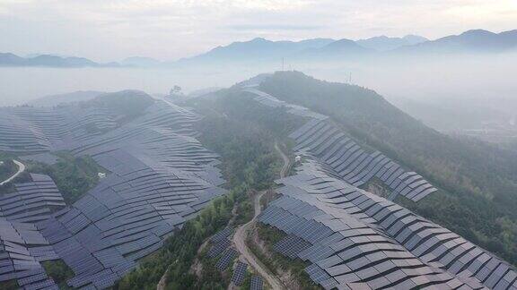 无人机在晨雾中观察起伏山坡上的太阳能发电厂