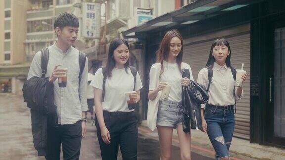 一群年轻的亚洲学生走在街上喝着珍珠奶茶(慢镜头)