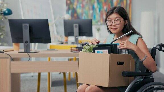 积极微笑开朗有魅力的年轻女性戴着眼镜残疾人坐在轮椅上并因此晋升到另一个职位手持纸板箱的东西配件