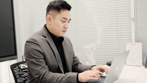 亚洲成熟的中国商人留着胡子打字回复客户的电子邮件在办公室用笔记本电脑与客户进行视频通话