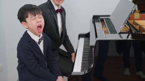 钢琴家在学校教一个男孩弹钢琴最喜欢的古典音乐孩子在钢琴教室里打呵欠身着正式优雅套装的音乐家教育、练习、放松的理念