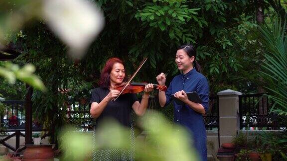 年轻的亚洲妇女教她的母亲如何在室外拉小提琴
