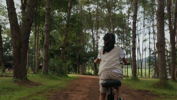 年轻的亚洲女孩在松林里骑自行车玩得很开心