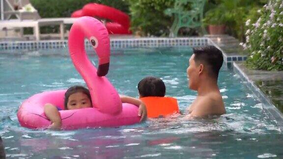 快乐的亚洲家庭带着充气或救生衣在酒店游泳池嬉戏享受夏日假期年轻的父亲、女儿和儿子一起在户外游泳池里放松