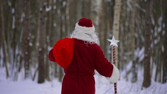 圣诞老人带着魔法杖和一袋圣诞礼物在雪林里后视图