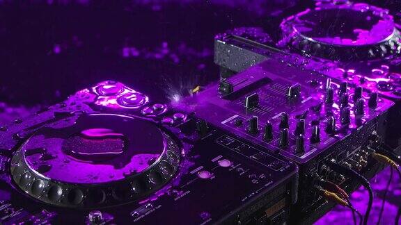 音频混音控制器在一个黑暗的工作室里紫色的照明DJ工具在倾盆大雨中前视图关闭了慢动作