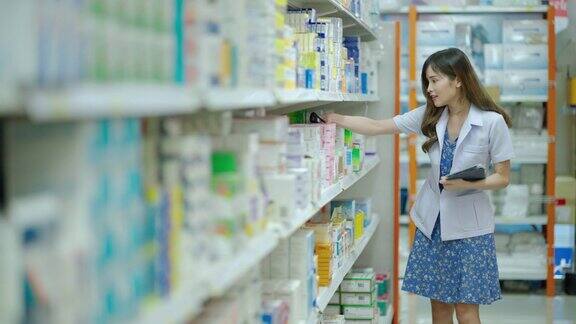 美丽的亚洲药剂师正在检查产品在现代药房哪个是有大量产品的零售商店