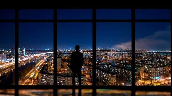 这个男人站在窗户旁边背景是夜晚的大都市时间流逝