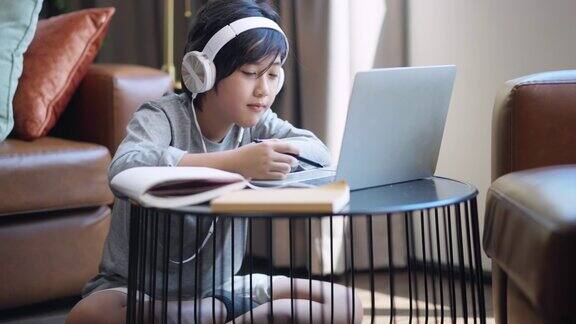 亚洲孩子男孩孩子接受电子学习学习在线课程从学校老师通过数字远程设备笔记本电脑互联网会议在客厅亚洲青少年戴着耳机使用笔记本电脑在家里学习课程