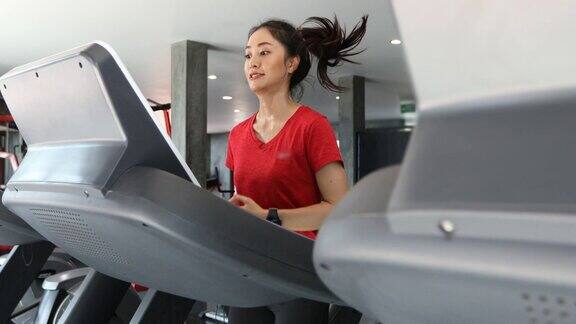 一名年轻的白人女性在跑步机上慢跑而亚洲女性在健身房里穿运动鞋