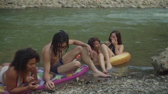 欢乐多元的多民族朋友穿着泳衣在河边的充气环上放松