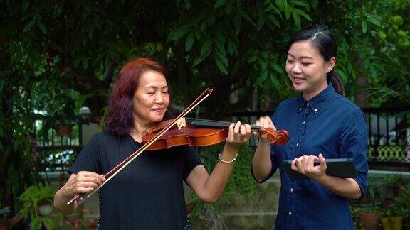 年轻的亚洲妇女教她的母亲如何在室外拉小提琴