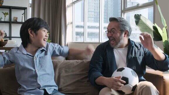 亚洲父亲和儿子在电视上看足球比赛当球队把球射进球门时他们高兴地激动起来
