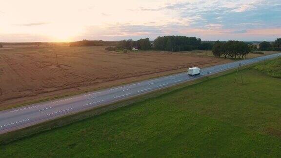 跟踪和航拍一辆卡车在高速公路上行驶美丽的田野风景和夕阳被看到