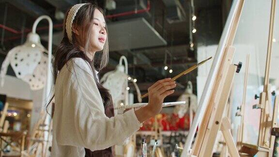 年轻的亚洲女艺术家在艺术工作室画日落风景画