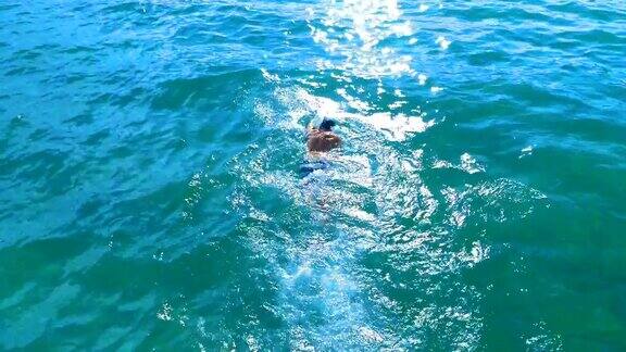 无人机的慢动作镜头一个年轻的健康男子在海里自由泳