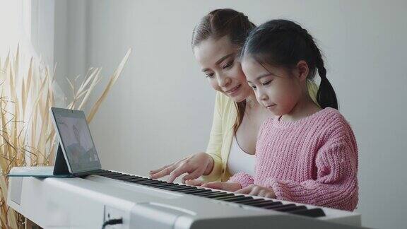 亚洲妈妈在家里教女儿弹钢琴一起快乐的家庭活动在线音乐学校业务概念视频会议