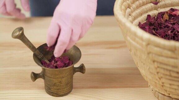女孩把干玫瑰花瓣从篮子里移到一个带杵的铜臼里制作天然磨砂膏的过程