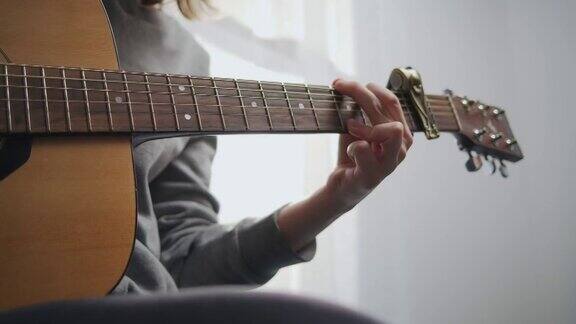 一个少年在明亮的房间里弹吉他房间里阳光灿烂这位艺术家弹吉他这女孩练习一种乐器特写镜头