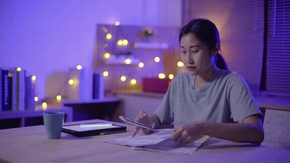年轻的亚洲女性晚上在家用手机支付账单