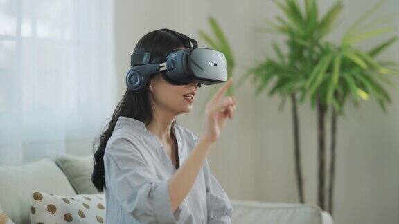 年轻的亚洲女性戴着VR眼镜坐在家里的沙发上