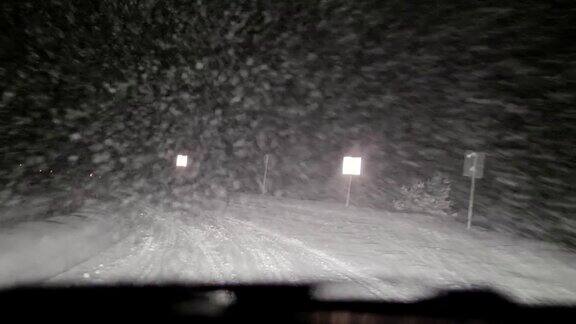 司机POV在积雪覆盖的道路上行驶初雪飘落被前灯和雪照亮的路