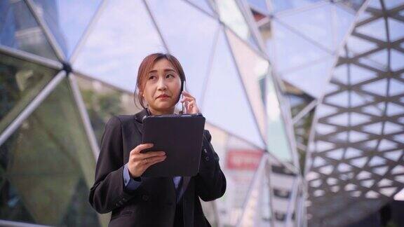 年轻的亚洲女商人在回到办公室工作时一边使用笔记本电脑一边用智能手机聊天