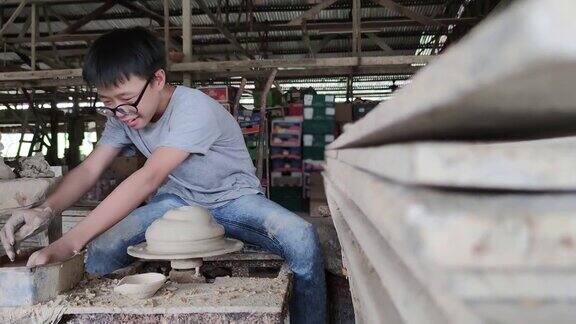 一个亚洲的中国少年正在陶轮上形成一个泥碗他高兴地展示他的产品产量