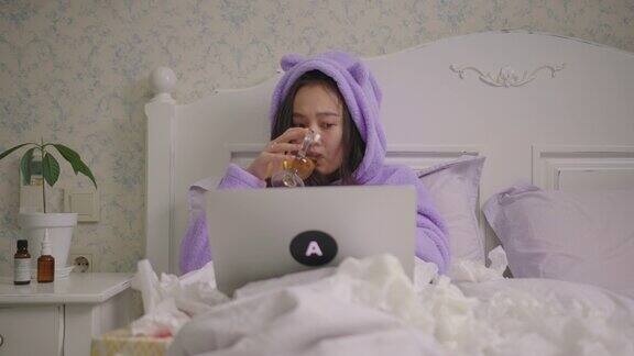 亚洲妇女喝热茶和看笔记本电脑躺在床上在家穿着紫色睡衣的女人在床上玩笔记本电脑