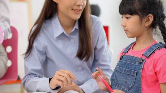 亚洲小女孩完成了在桌子上的彩色书和在教室里与老师击掌多民族学前年轻的亚洲教师和学生在教室里幼儿园和学习理念