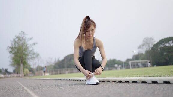 一名亚洲妇女在草地旁的跑道上系鞋带