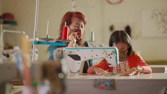 亚裔华裔女教师在工作室教育课上指导年轻女学生用缝纫机缝制蜡染布防护口罩