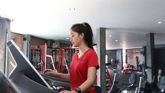 一名年轻的白人女性在跑步机上慢跑而亚洲女性在健身房里穿运动鞋