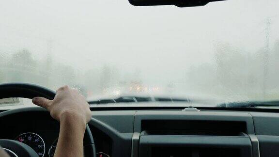 一位妇女在大雨中开车后视图在方向盘和挡风玻璃的框架挡风玻璃刮水器