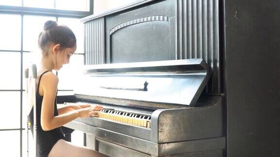4K视频选择拉移焦点中拍摄侧视图的年轻美丽的小女孩在黑色紧身衣坐在和弹钢琴与乐谱笔记平板在工作室的玻璃墙前