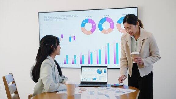 年轻的亚洲女商人在会议室里和同事在电脑屏幕上讨论财务图表和市场营销