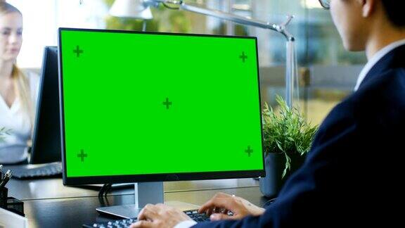在办公室里商人在一台模拟绿色屏幕的台式个人电脑上工作同事走进办公室并在她的办公桌前发生