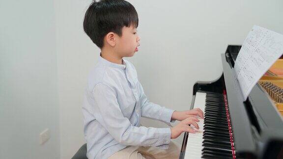 亚洲男孩穿着衬衫在学校的教室里弹钢琴孩子在课堂上看着纸笔记玩得很开心教育、技能和学习观念音乐家钢琴练习