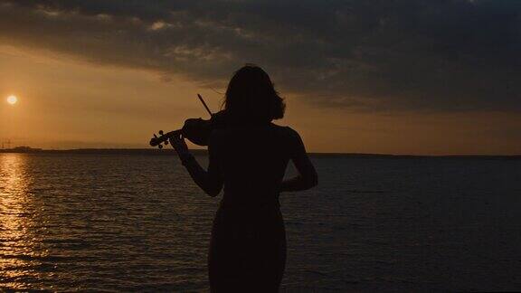 女小提琴手在湖岸演奏的剪影