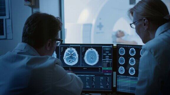 在控制室医生和放射科医生讨论诊断同时观看程序和显示器显示的大脑扫描结果在背景患者接受MRI或CT扫描程序