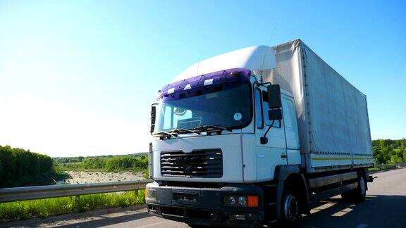 在阳光明媚的日子里在高速公路上行驶的带有货物拖车的大卡车白色卡车穿过乡村公路驶向目的地美丽的背景慢动作侧视图特写