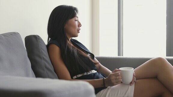 年轻的亚洲女商人在沙发上休息喝着咖啡