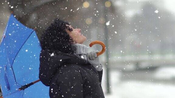 美丽的年轻女子卷着头发打着伞在雪中享受雪花在她的脸上
