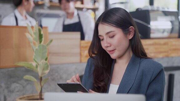 亚洲女性坐在咖啡店使用笔记本电脑和数字平板电脑开始新的业务