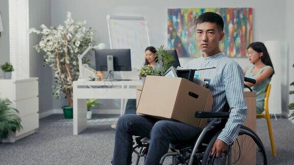 残疾男子雄心勃勃的衬衫与亚洲韩国美女坐在轮椅在公司的桌子上膝盖抱着纸箱包装的东西被解雇的工作无法履行他的职责