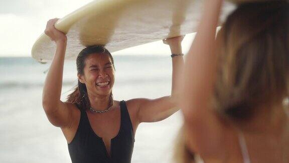 4K亚洲女性朋友拿着冲浪板一起走在热带海滩在夏日日落